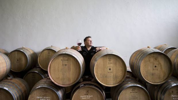 Andy Anderson standing behind wine barrels