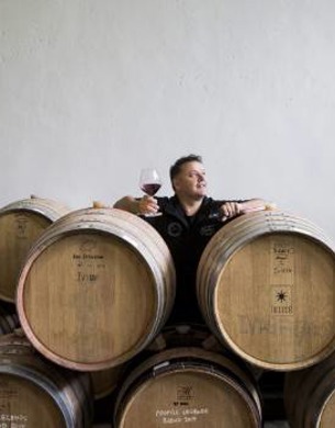 Andy Anderson standing behind wine barrels