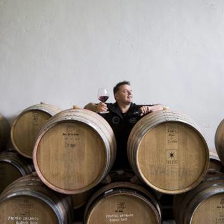 Andy Anderson standing behind wine barrels