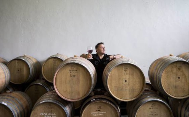 Andy Anderson standing behind wine barrels