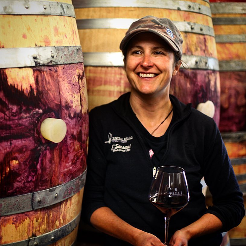 Jen Parr holding a glass of red wine next to barrels