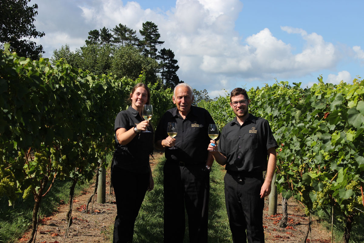 The Soljians holding glasses of white wine in a vineyard