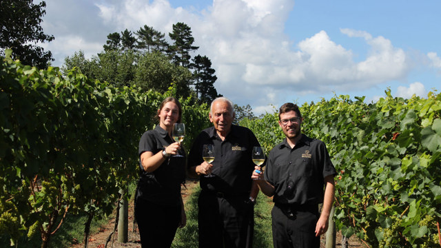 The Soljians holding glasses of white wine in a vineyard