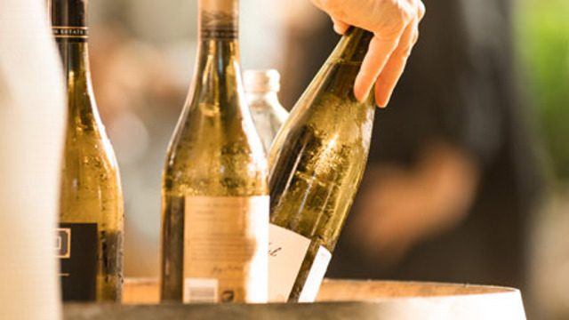 A wine bottle being picked up from a top of a barrel.