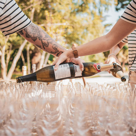 Multiple people pouring sparkling wine into a large amount of glasses.
