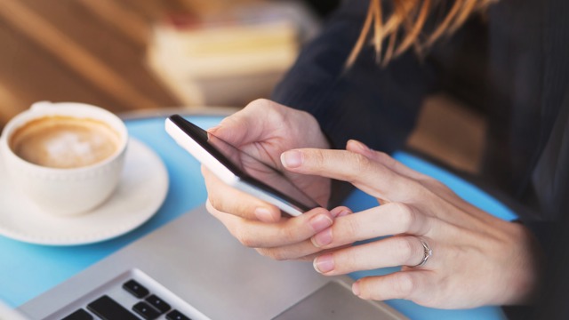 A woman using a smartphone with a coffee next to her.
