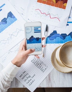 A person holding coffee while looking at stats on a smartphone and documents