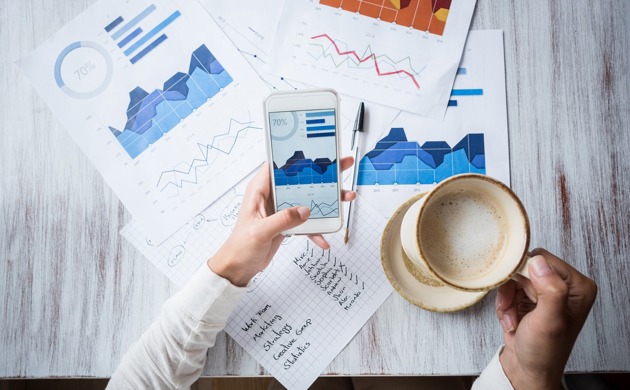 A person holding coffee while looking at stats on a smartphone and documents
